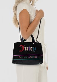 Borsa a mano nera con testo ricamato multicolore "Juicy" e "Est. Los Angeles." Presenta due manici e una tracolla regolabile.