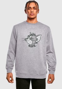 Grå sweatshirt med lange ermer og ribbestrikkede mansjetter. Har et trykt hode av Tom-karakteren og ordet "NEI" i fet svart tekst under.
