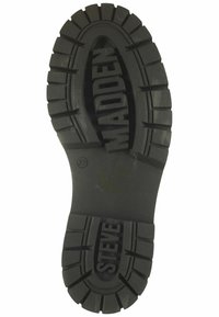 Suela de zapato de goma negra con surcos profundos, logotipos en relieve de "STEVE" y "MADDEN", y un indicador de tamaño "37" cerca del área del tacón.