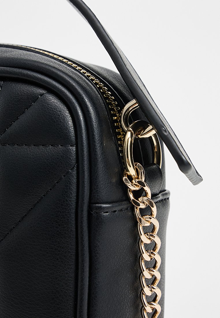 Bolso de cuero negro con un diseño acolchado, cierre de cremallera dorada y correa de cadena. Presenta una forma elegante y una textura suave.