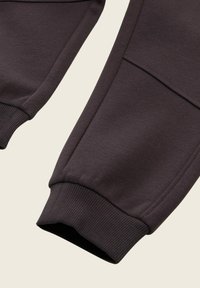 Mörkbruna sweatshirtbyxor har ribbade muddar, en slät tygstruktur och en lätt lyster, med framfickor och en avslappnad passform.
