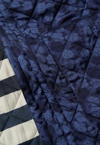 Gros plan d'un quilt avec des motifs floraux bleu marine et des rayures diagonales noires et blanches, montrant des coutures détaillées et la texture du tissu.