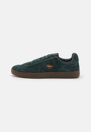 Grønne sued sneakers med en teksturert finish, brun gummisåle og en liten oransje logo på siden. Snøring og lavt snitt.
