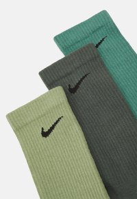 Tre par ribbede Nike sokker i varierende nyanser: lys grønn, mørk grønn og teal, med svarte Nike swoosh-logo aksenter.
