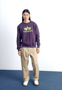 Maroon sweatshirt with yellow logo, beige pants, and white shoes. The sweatshirt has ribbed cuffs and hem; the pants are loose-fitting.