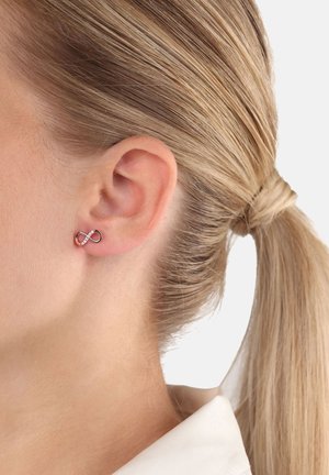 Ohrringe mit unendlichem Symbol aus roségold mit klaren Akzenten, die eine glatte Oberfläche und minimalistisches Design aufweisen, seitlich an einem Modell gezeigt.