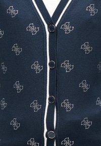 Μπλε ναυτικό ζακέτα με λευκή επένδυση, που διαθέτει λαιμόκοψη V, διακοσμητικά κουμπιά και μοτίβο από μικρές ασημένιες-καθρεφτισμένες λεπτομέρειες σε όλο το ύφασμα.