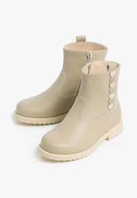 Beige leather ankle boots with a side zipper, textured surface, and heart-shaped accents along the back. Light-colored rubber sole.