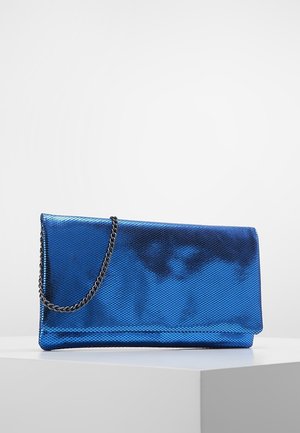 Pochette bleue brillante à texture, avec une bandoulière en chaîne noire métallique, exposée sur un socle blanc sur un fond clair uni.