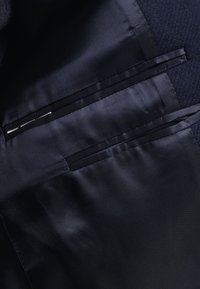 Granatowa podszewka marynarki z dwiema wszytymi wewnętrznymi kieszeniami wykończonymi polerowaną tkaniną.