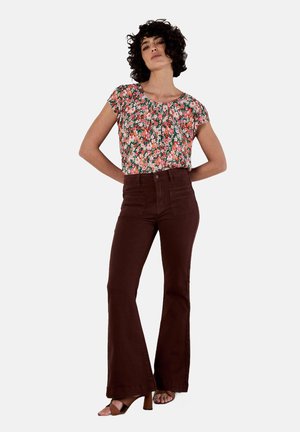Camicetta floreale a maniche corte nelle tonalità di rosa, arancione e verde. Pantaloni marroni a vita alta e svasati completano l'outfit, abbinati a tacchi marroni.