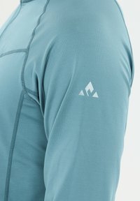 Pitkähihainen paita vaaleansinisestä materiaalista, jossa on teksturoitua ommelta. Läpivärillä oleva geometrista logoa valkoisella olkapäässä. Liukas, istuva muotoilu.
