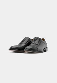 Zapatos de vestir de cuero negro con acabado suave, punta redonda y un diseño simple de cordones. Presentan un ligero tacón y costuras decorativas.