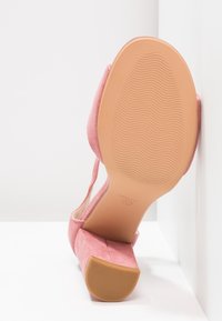 Chaussure à talon haut en daim rose, posée sur son talon, semelle visible avec une empreinte à motif de vagues, taille 37, sur fond blanc.