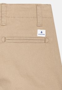 Pantalon en tissu coton beige avec poche arrière, passants de ceinture et une petite étiquette de marque Jack & Jones blanche et bleue.