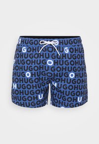 Tengeri rövidnadrág kék háttérrel, fekete és fehér "HUGO" mintázattal, rugalmas derékpánttal és zsinóros zárással.