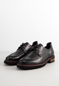 Chaussures de ville en cuir noir avec des surfaces lisses et texturées, lacées, à bout rond, et avec des accents de semelle marron contrastante.