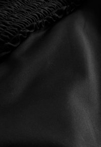 Tissu noir avec une texture lisse, présentant un détail froncé sur le bord supérieur et une finition douce et mate qui s'étend en dessous.