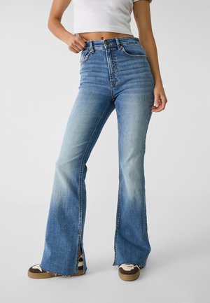 High-waisted flared jeans in light blue denim, featuring front pockets, side slits at the hem, and a faded design with stitching details.