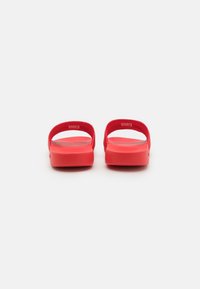 Sandalias rojas de tira con la espalda abierta, material de textura suave, diseño minimalista y una tira delgada en la parte superior.