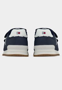 Μπλε ναυτικό αθλητικό παπούτσι με λευκή ταμπέλα στη φτέρνα, λουριά βέλκρο και υφή στη σόλα από καουτσούκ. Διαθέτει λογότυπο πάνω από τη φτέρνα.