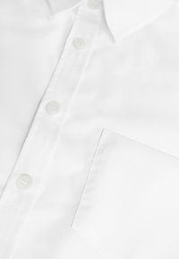 Weißes Hemd mit Knöpfen, das eine glatte Textur, einen spitzen Kragen, fünf Knöpfe und eine Brusttasche auf der linken Seite aufweist.