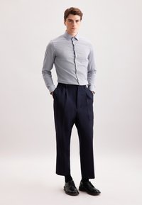 Camicia button-up a righe blu chiaro abbinata a pantaloni a pieghe blu navy scuri e scarpe stringate nere. Design e vestibilità semplici e su misura.