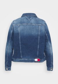 Jeansjacka med en gradientblå tvätt, klassisk krage, knappribbor och en logotypapplikation med röda, vita och blå accenter längst ner.