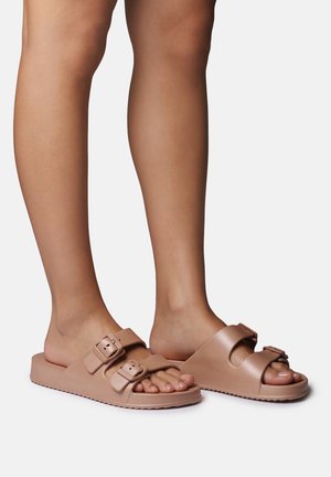 Heledad helepruunid libisesaapad, valmistatud siledast sünteetilisest materjalist, millel on kaks reguleeritavat pandlaga rihma. Põhjaks on lame tekstuurse põhjaga tall.