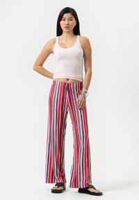 Pantalons larges à rayures avec des lignes horizontales rouges, bleues et beige. Associés à un débardeur rose ajusté et des sandales noires.