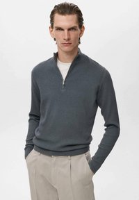Grau gerippter Pullover mit hohem Reißverschlusskragen,Slim Fit und weicher Textur, kombiniert mit hellen Hosen.