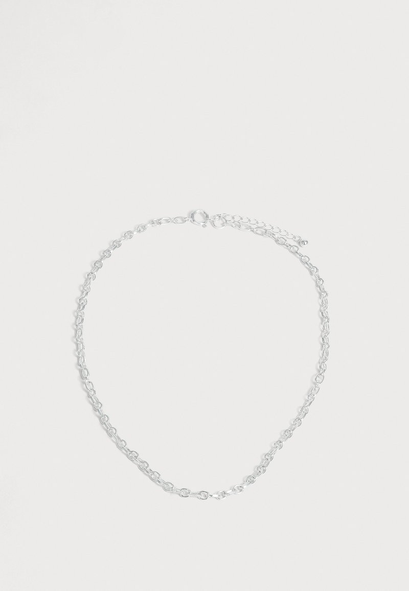 Fin collier chaîne en argent avec des maillons ovales et un petit fermoir ajustable, présenté sur un fond blanc uni.
