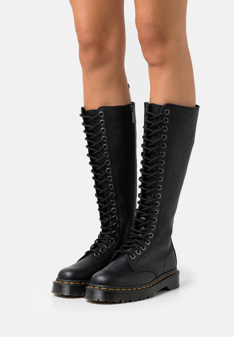 Bottes noires en cuir montantes à lacets avec une finition texturée, semelle en caoutchouc épaisse et œillets métalliques. Dispose d'une fermeture éclair sur le côté.