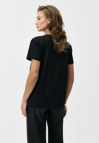 Czarny bawełniany t-shirt z krótkim rękawem, o luźnym kroju, okrągłym dekolcie i gładkim wzorze. Noszony z ciemnymi spodniami.