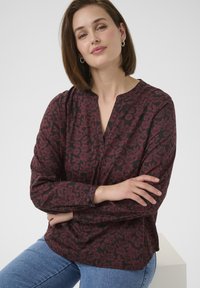 Langsleeve shirt met een diep bordeauxrode bloemenpatroon op een donkere achtergrond, voorzien van een v-halslijn en met knoopsluiting aan de mouwen. Zachte stof, relaxte pasvorm.