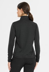 Zwart langwerpig shirt met lange mouwen van gestructureerde stof, met een hoge kraag en een gebogen zoom. Heeft contrasterende stiksels langs de zijkanten.