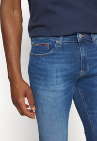 Modré džíny z denimu se střihem na rovno, s klasickým designem pěti kapes a jemným červeným prošitím na přední kapse.