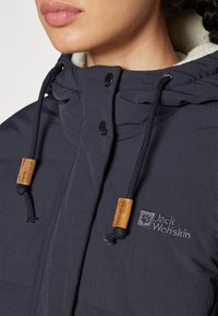 Giacca piumino blu navy realizzata in tessuto testurizzato. Dotata di cappuccio, coulisse e patch con logo, con chiusura a bottoni a pressione.