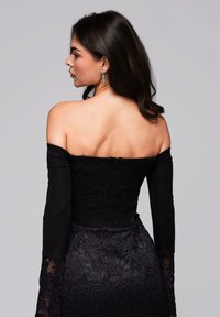 Abito nero in pizzo senza spalline con maniche lunghe e aderenti, motivo floreale intricata e una silhouette aderente, dotato di chiusura con zip sul retro.