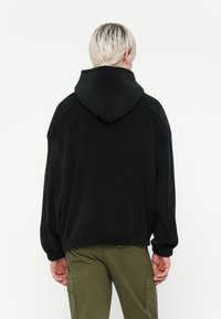 Zwarte capuchontrui met een comfortabele pasvorm, gemaakt van zacht materiaal. Heeft een geribde zoom en boorden. De achterkant heeft geen duidelijke patronen.