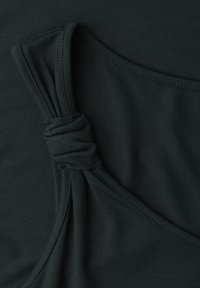 Tessuto verde scuro con dettaglio nodo cucito e linee di cucitura visibili su una superficie tessile liscia.
