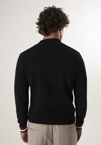 Maglione nero a maglia con una trama testurizzata, caratterizzato da un colletto a coste e dettagli a strisce in rosso e bianco nei polsini. Vista posteriore mostrata.