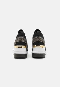 Schwarze Strick-Sneaker mit strukturiertem Muster, metallischen goldenen Akzenten an der Ferse und einem weißen und schwarzen Sohlen-Design.