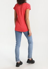 Červené tričko s krátkými rukávy a volnějším střihem, doplněné světle modrými úzkými džíny a černými botami. Látka má texturovaný, melírovaný vzhled.