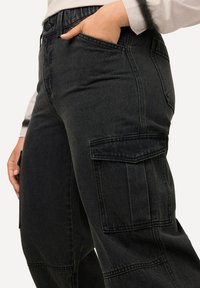 Pantalones cargo de mezclilla negra con un ajuste relajado, que cuentan con bolsillos laterales, piernas anchas y una tela texturizada. Cintura elásticada para mayor comodidad.