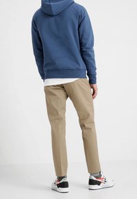 Blå luvtröja med känguruficka, kombinerad med ljusbeige, tajta byxor och svartvita sportskor med röda detaljer.