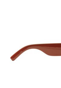 Brązowe okulary przeciwsłoneczne o smukłym, zakrzywionym kształcie. Wykonane z błyszczącego plastiku, z subtelnie umieszczonym oznaczeniem CE blisko zawiasu.