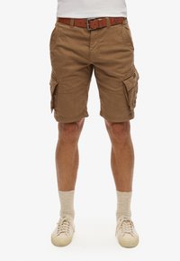 Bruine cargoshorts van katoen, met meerdere zakken en stikdetails; gedragen met een bruine riem en lichtgekleurde sneakers met sokken.
