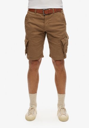 Brune cargo shorts lavet af bomuld, med flere lommer og sømdetaljer; iført med et brunt bælte og lyse sneakers med sokker.