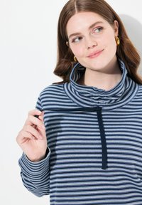 Maglione a righe navy e azzurro chiaro, con un alto colletto, zip a un quarto e tessuto testurizzato. Maniche lunghe con dettagli ai polsini.